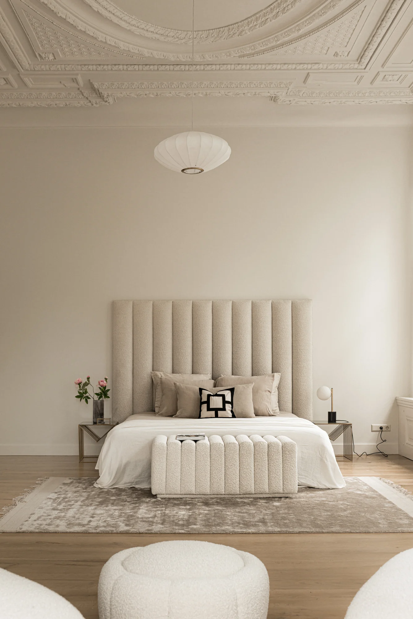 Luxe, minimalistisch ingerichte slaapkamer aan de Weteringschans met een hoog gestoffeerd bed, elegante ornamentenplafonds en zachte, neutrale tinten.