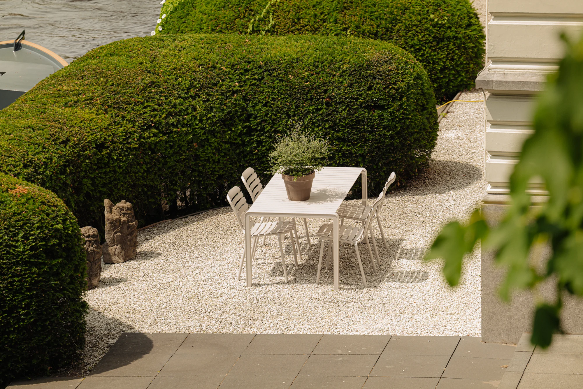 Witte tuintafel met zes stoelen en een plant erop, geplaatst op een grindterras aan de Weteringschans.