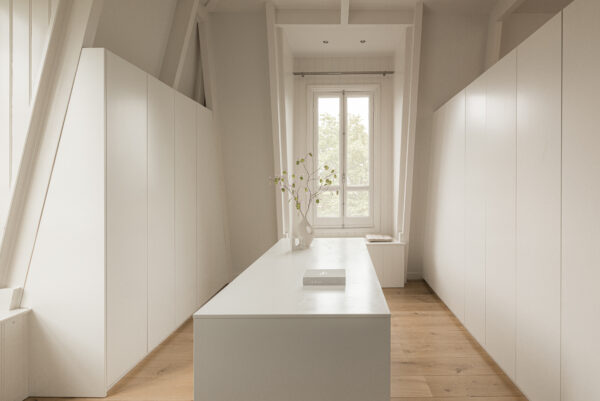 Minimalistisch, licht interieur van een moderne inloopkast aan de Weteringschans met witte kasten, houten vloer en een centraal eiland.