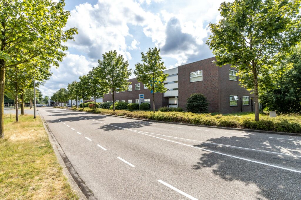 Bedrijfsgebouw aan de Terminalweg met bomen langs een rustige, brede weg op een zonnige dag.