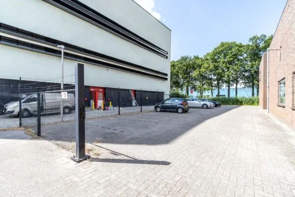 Parkeerterrein aan de Terminalweg met geparkeerde auto's naast een modern bedrijfsgebouw en een omheind terrein.