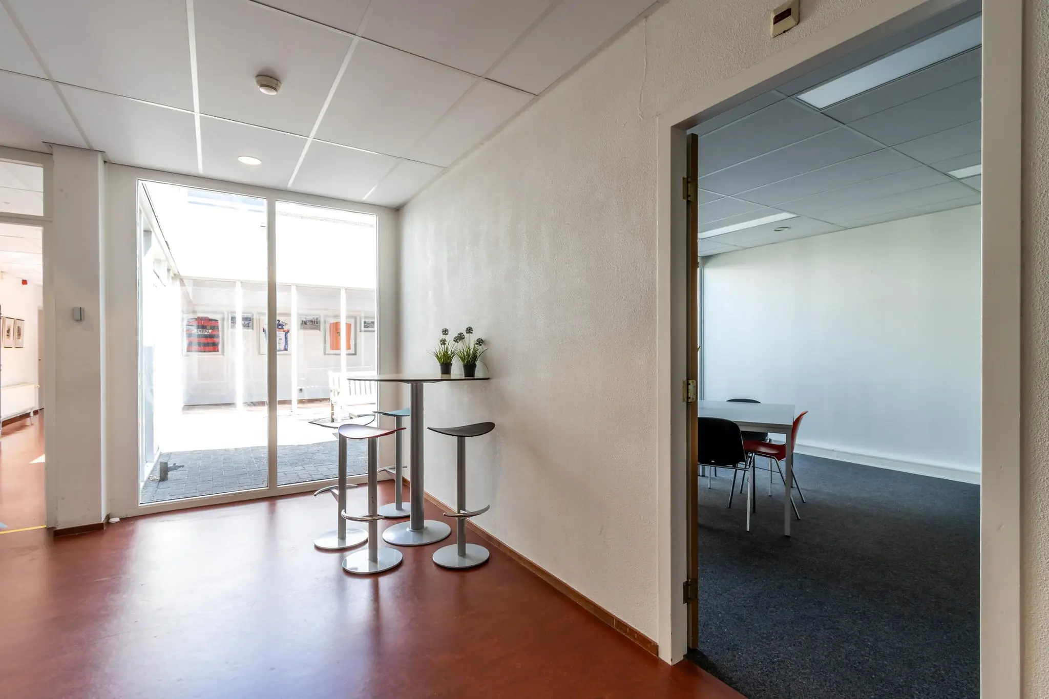 Hal met hoge tafel en barkrukken bij Terminalweg, met zicht op vergaderruimte en binnentuin.