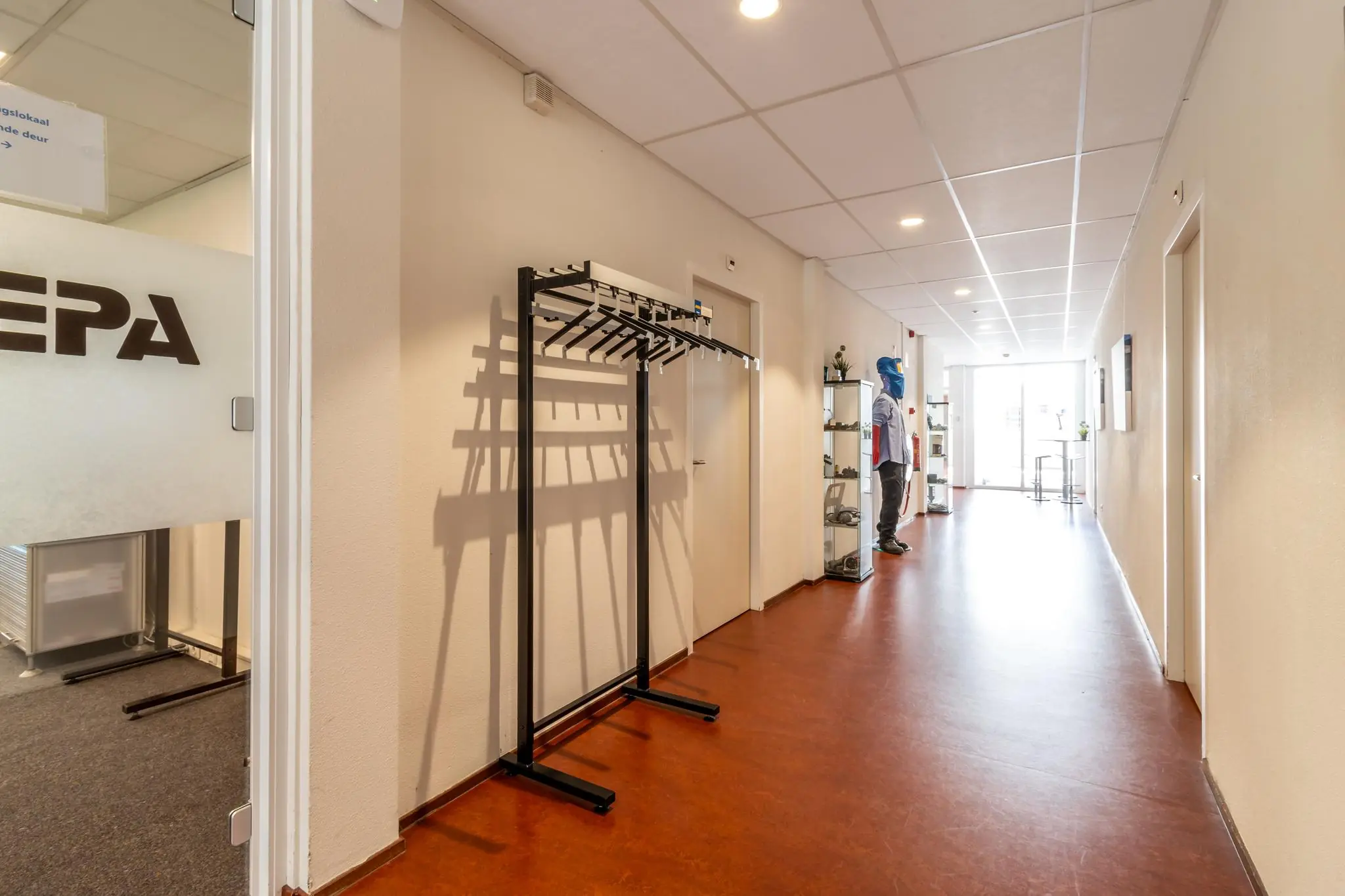 Lichte gang in een kantoorpand aan de Terminalweg met kapstok, vitrinekasten en een etalagepop in werkoutfit.