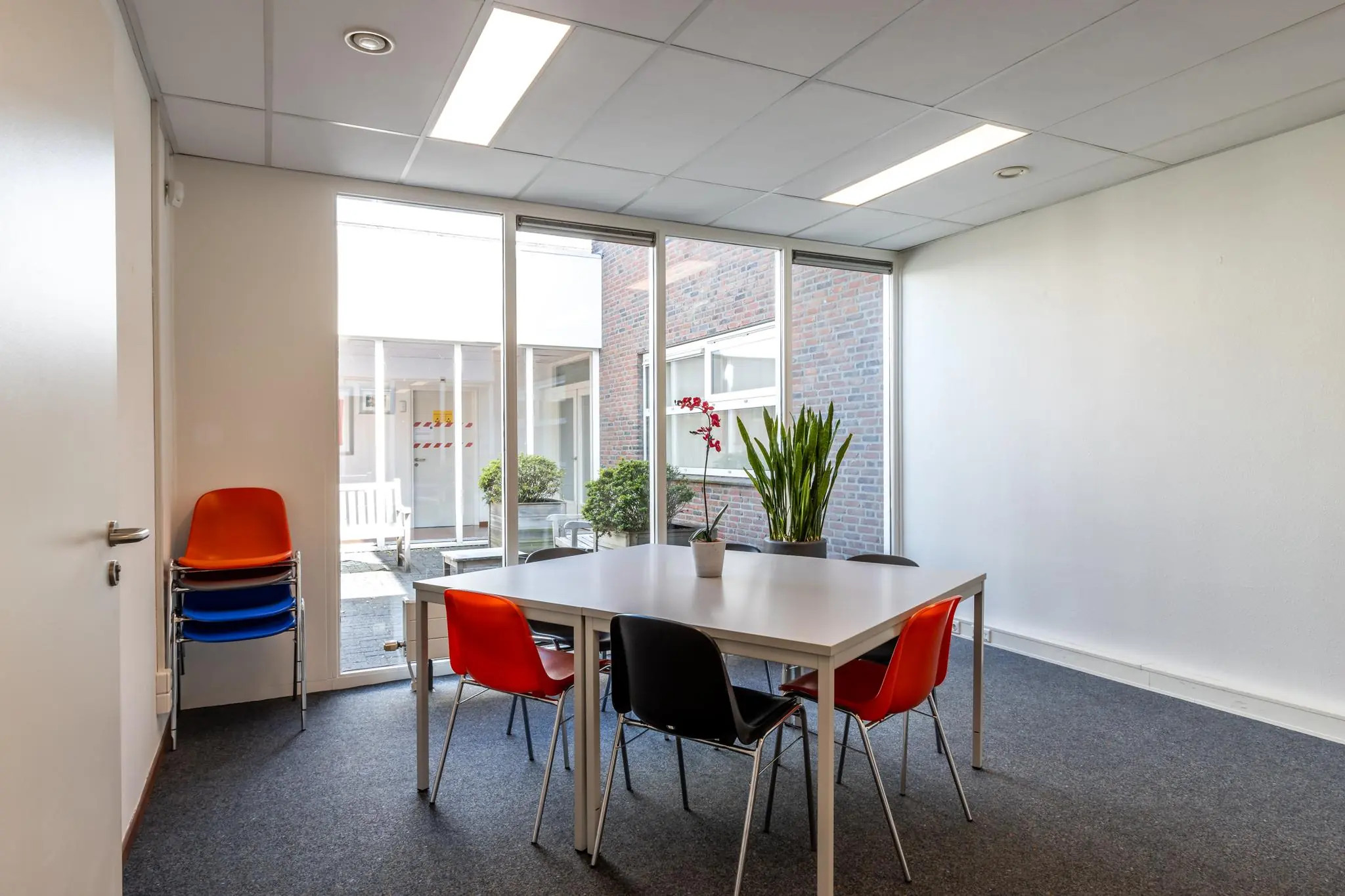 Vergaderruimte aan de Terminalweg met modern meubilair, kleurrijke stoelen en grote ramen met uitzicht op een binnenplaats.
