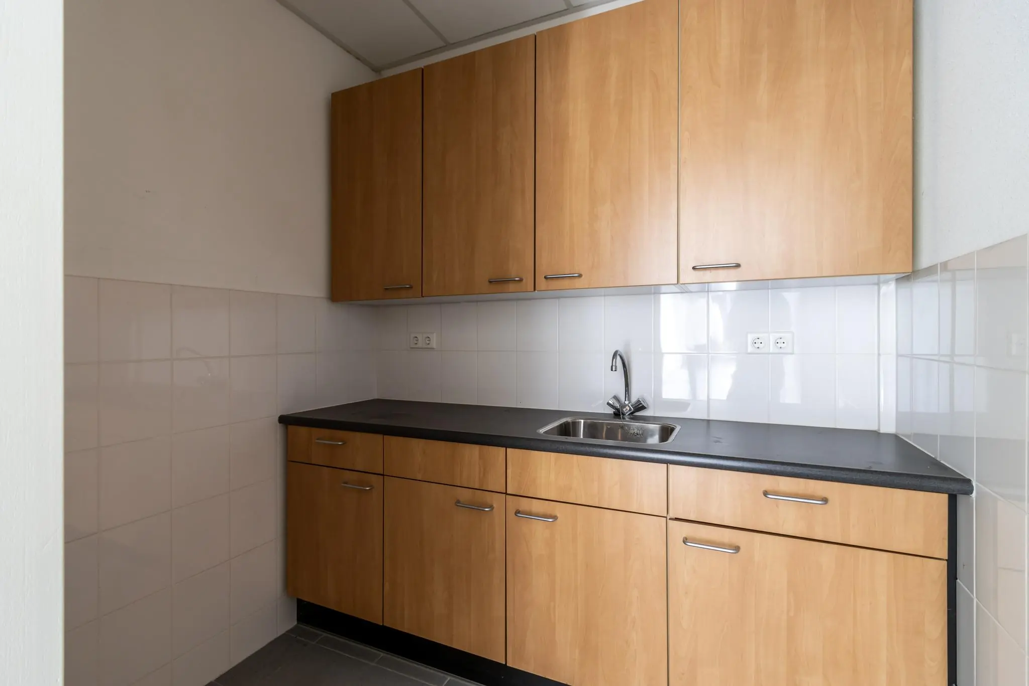 Keukenblok met houten kastjes, een zwart werkblad en een rvs-spoelbak in een bedrijfsruimte aan de Terminalweg.