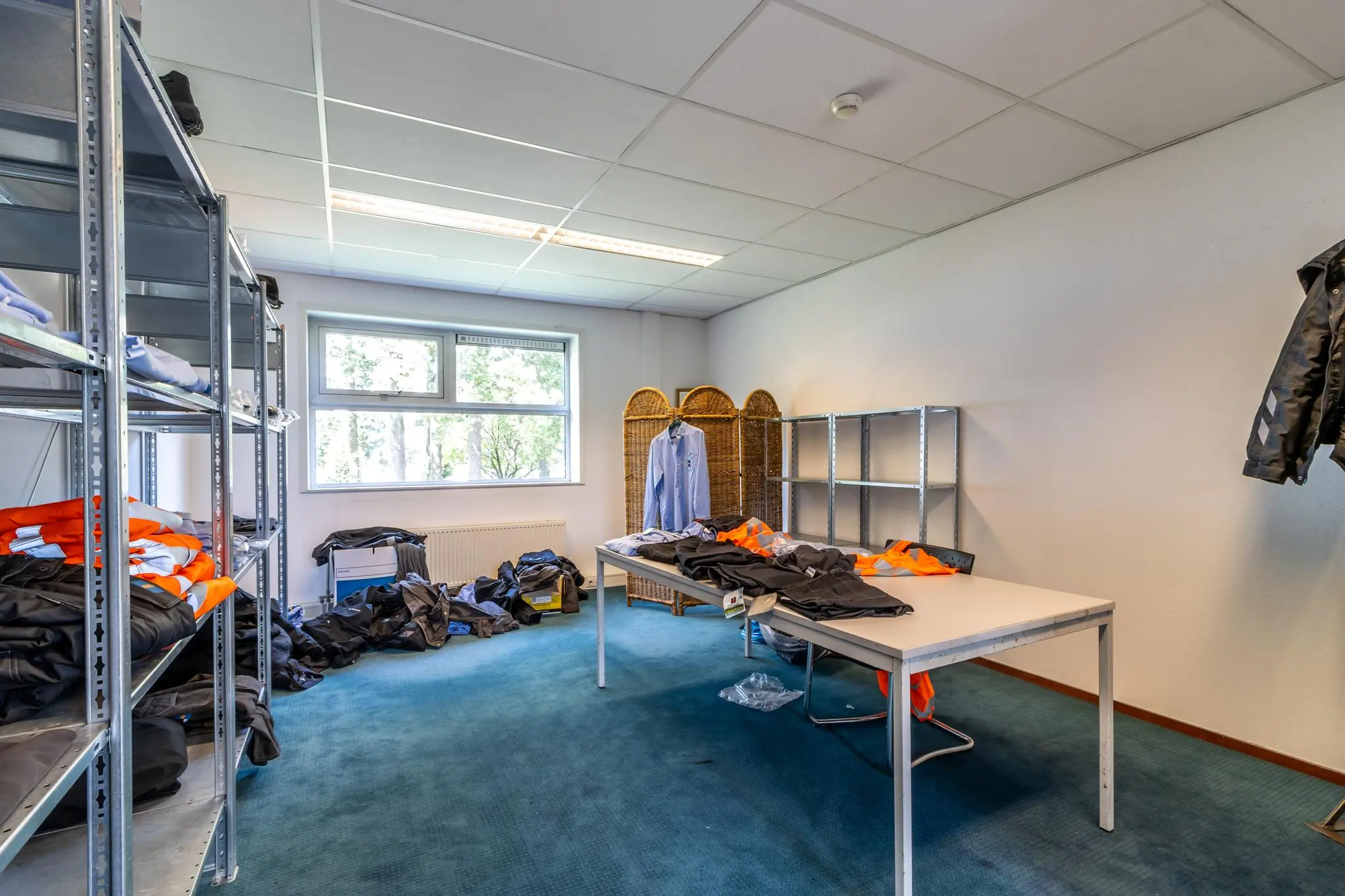 Kamer met metalen rekken, tafels en werkkleding in een bedrijfsruimte aan de Terminalweg.