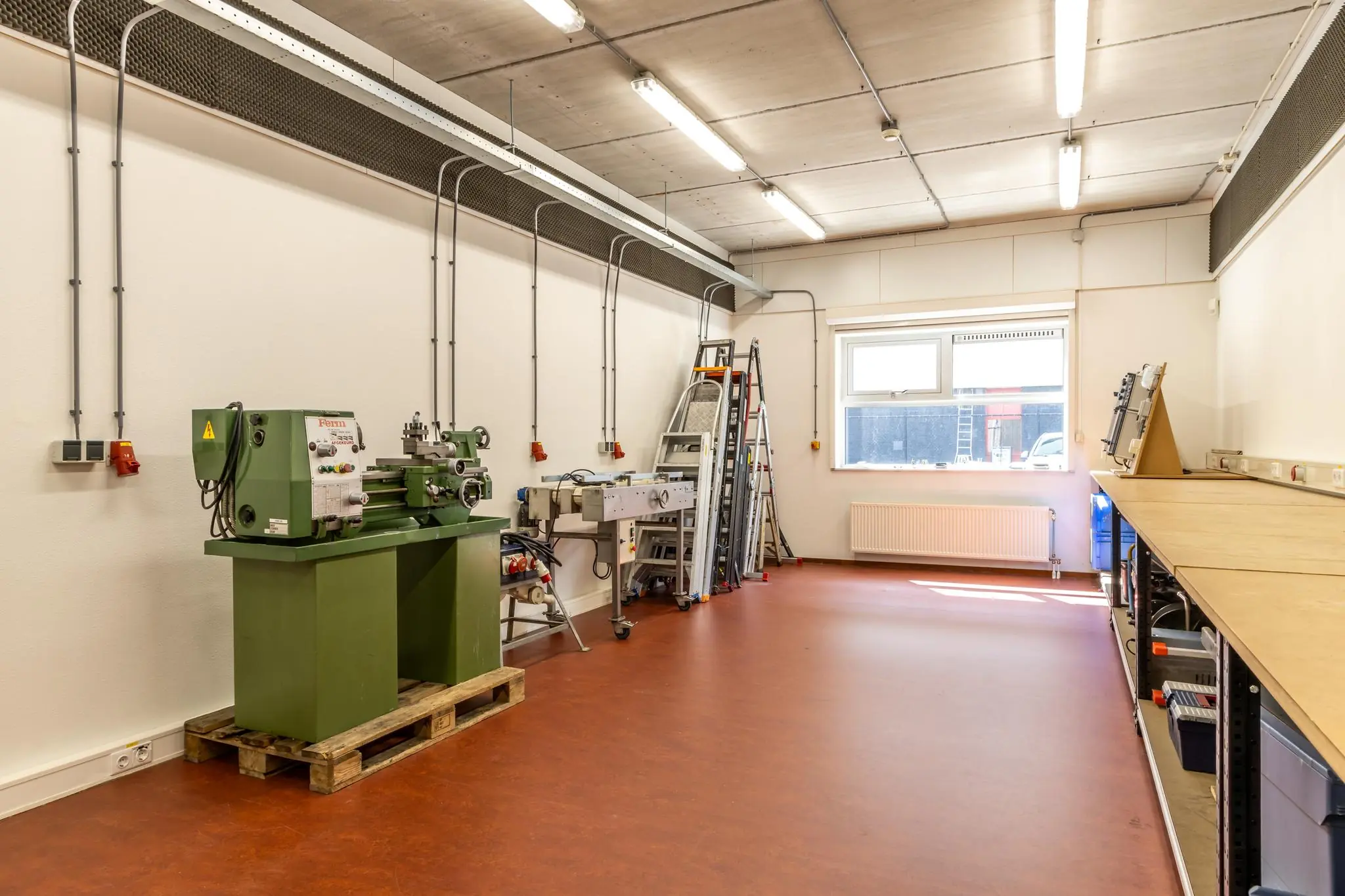 Licht werkatelier aan de Terminalweg met machines, werkbanken en opgestapelde ladders.