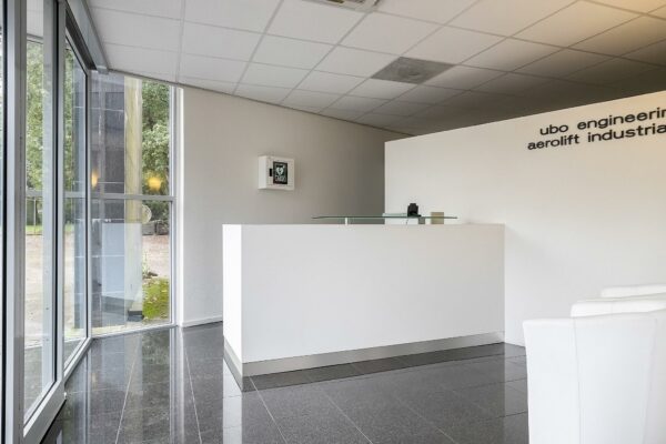 Moderne, minimalistische ontvangsthal van UBO Engineering en Aerolift Industrial aan de Banningstraat met witte balie en glazen gevel.