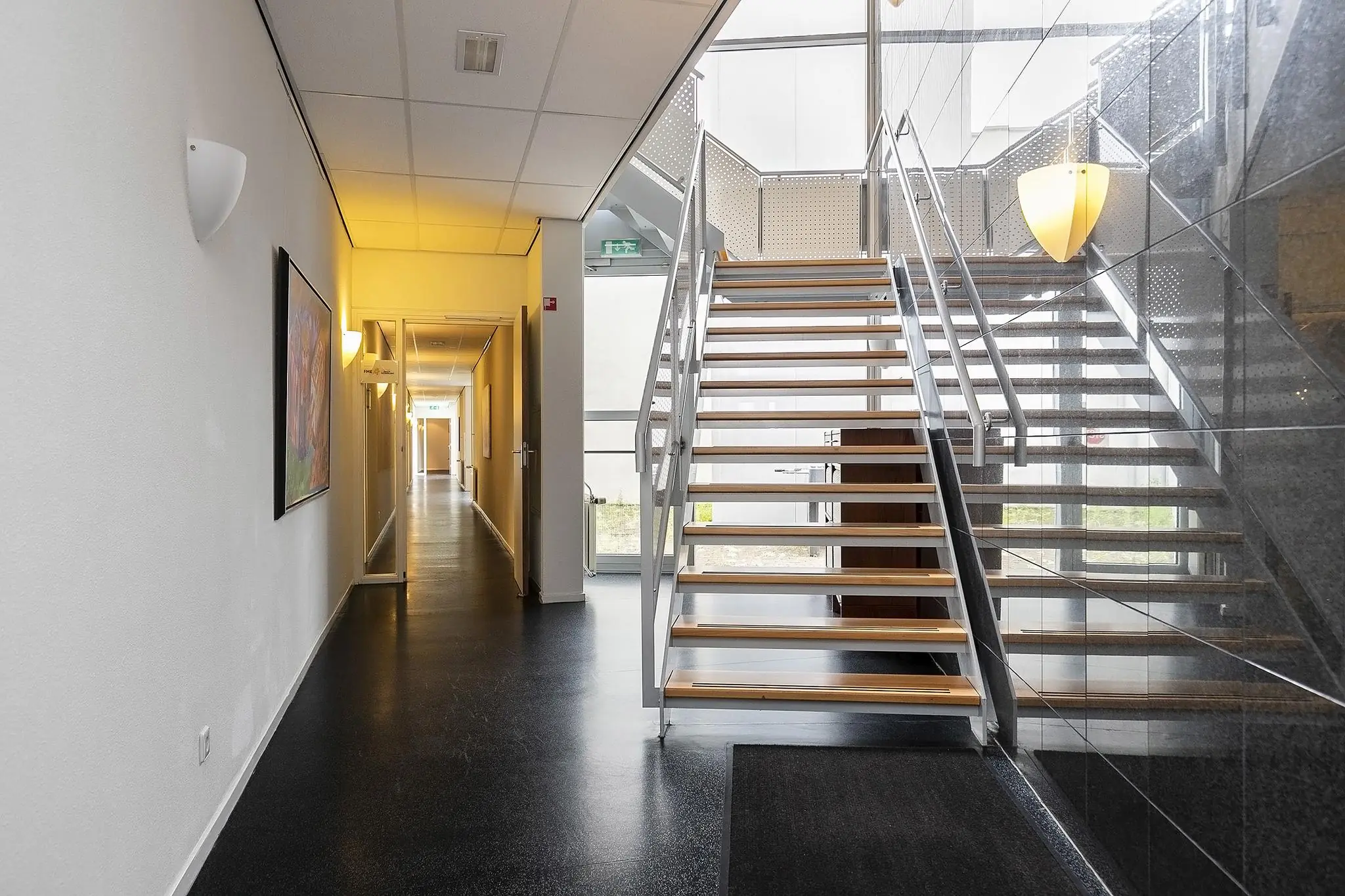 Moderne, lichte hal met een houten trap en een lange gang in een gebouw aan de Banningstraat.