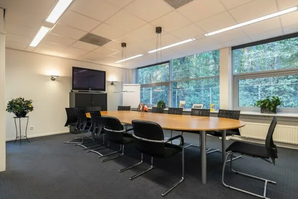 Vergaderruimte aan de Banningstraat met ovale tafel, zwarte stoelen, grote ramen en een flatscreen aan de muur.