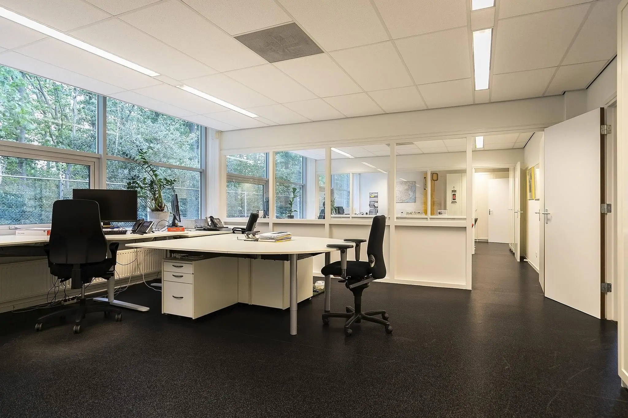 Modern kantoorinterieur aan de Banningstraat met werkplekken, bureaustoelen en grote ramen met uitzicht op groen.