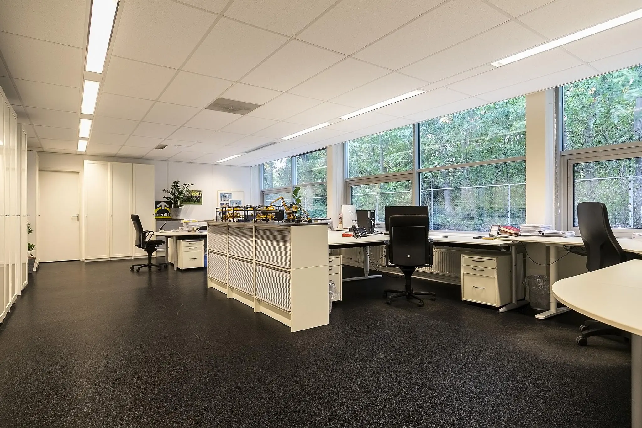 Modern kantoor aan de Banningstraat met meerdere bureaus, grote ramen en zicht op groen buiten.
