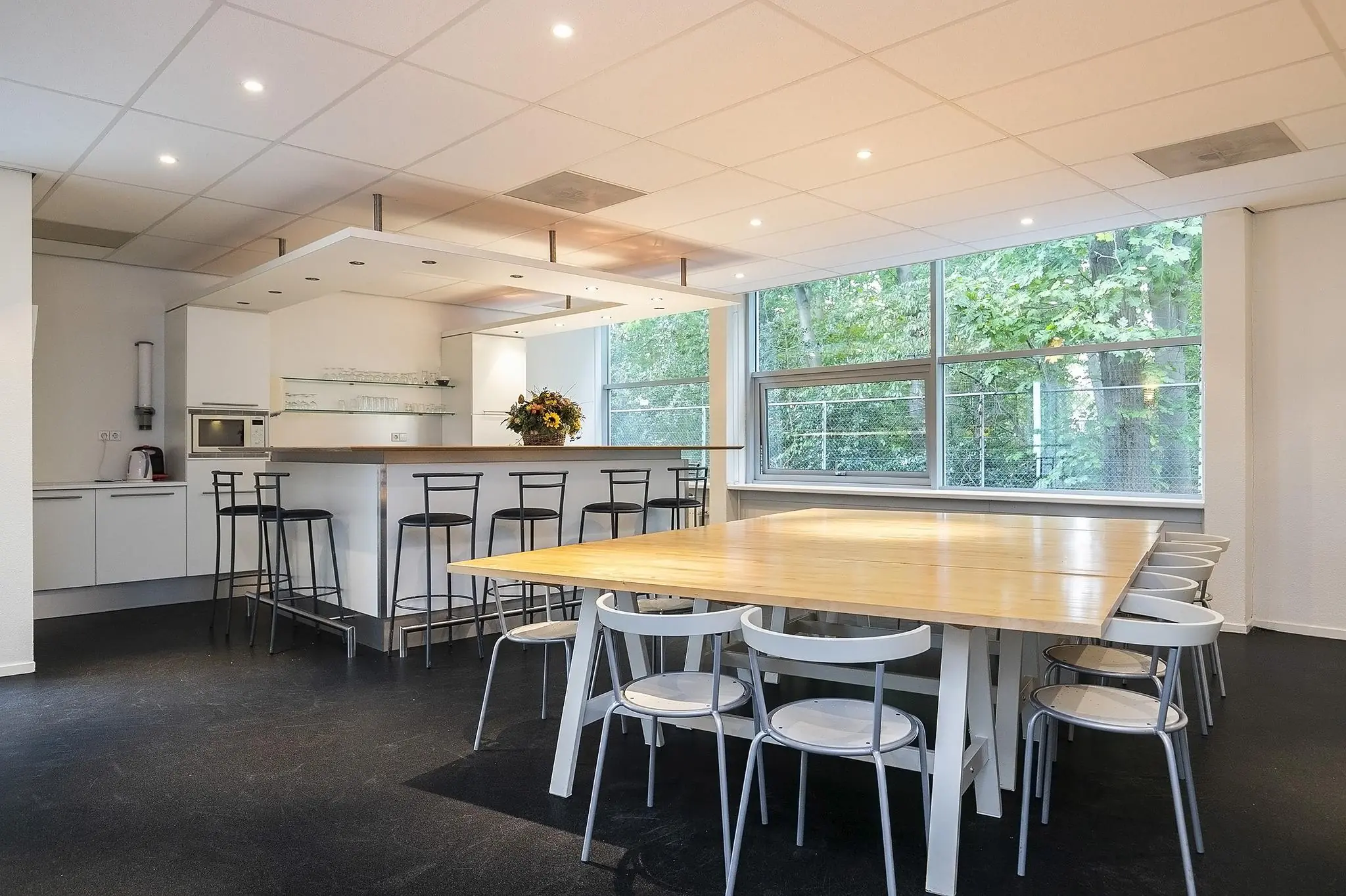 Moderne gemeenschappelijke keuken en eetruimte aan de Banningstraat met een bar, hoge en lage zitplaatsen en grote ramen met uitzicht op groen.