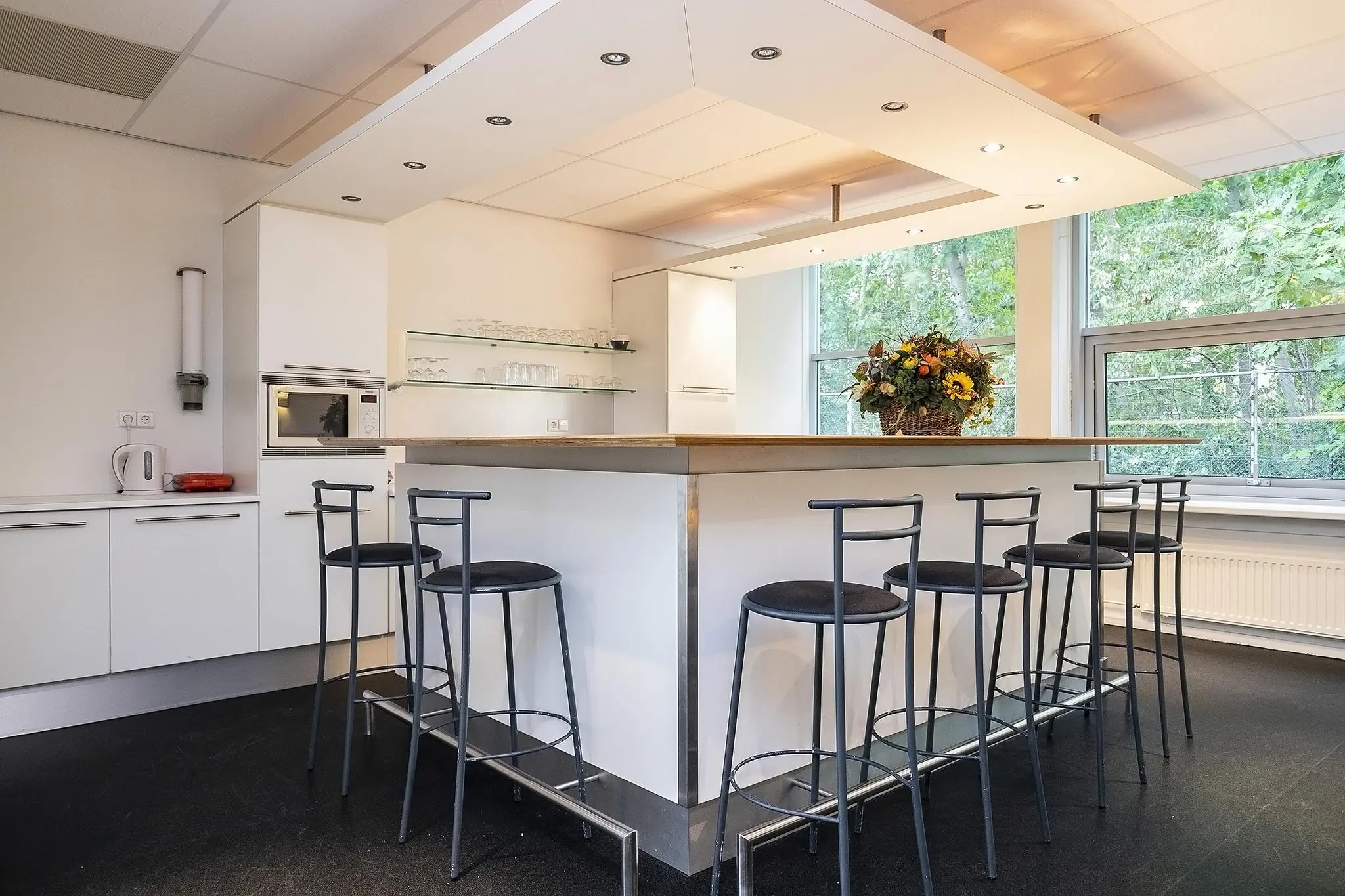 Moderne witte keuken met een kookeiland, barkrukken en een grote bloemenvaas bij het raam aan de Banningstraat.