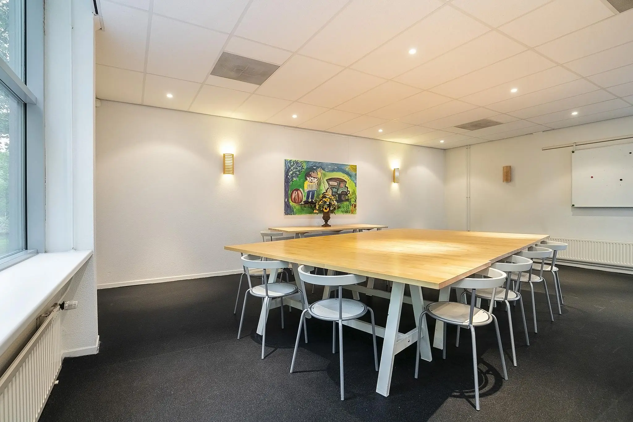 Vergaderruimte aan de Banningstraat met een grote houten tafel, witte stoelen, kunst aan de muur en een whiteboard.