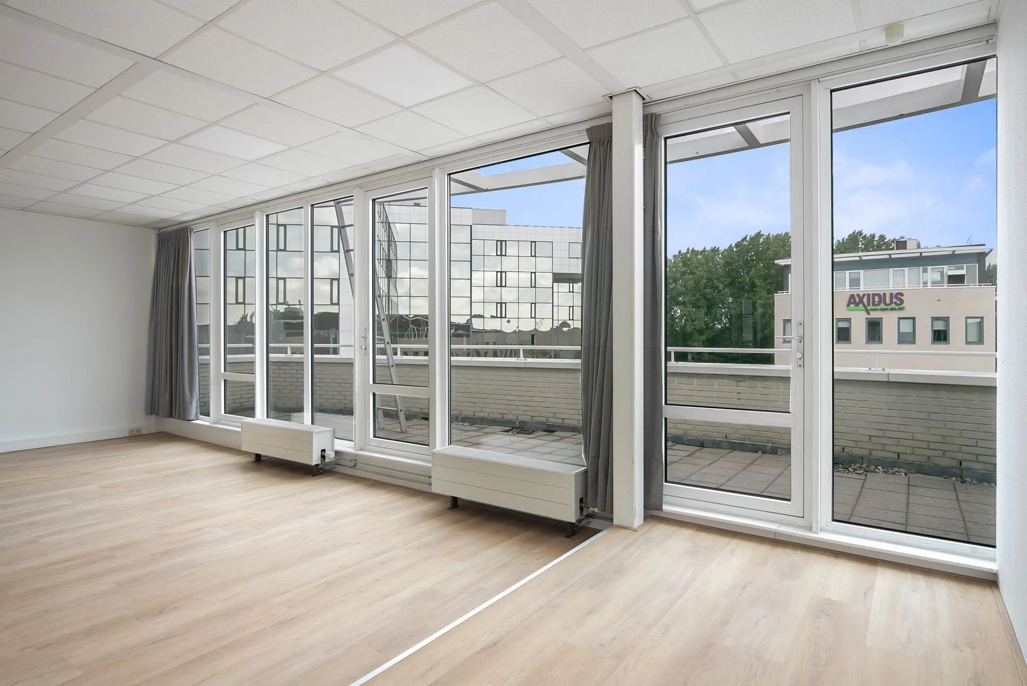 Lichte, leegstaande kantoorruimte aan de Cypresbaan met grote ramen en uitzicht op het Axidus-gebouw.