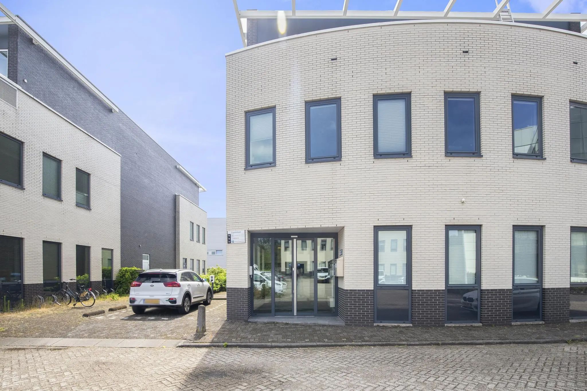 Vooraanzicht van een modern kantoorgebouw aan de Cypresbaan met parkeerplaats en fietsenrekken.