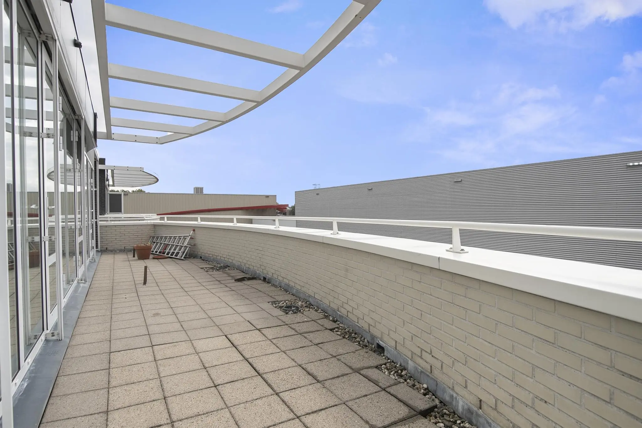 Ruim betegeld dakterras aan de Cypresbaan met glazen schuifpuien en wit metalen hekwerk.