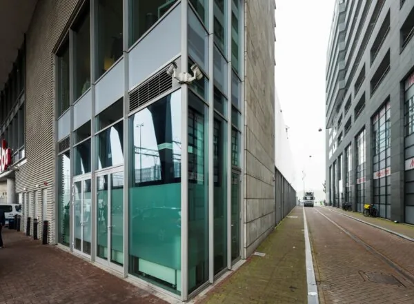 Straatbeeld van de Oosterdoksstraat in Amsterdam met moderne kantoorgebouwen en een smalle doorgang tussen de panden.
