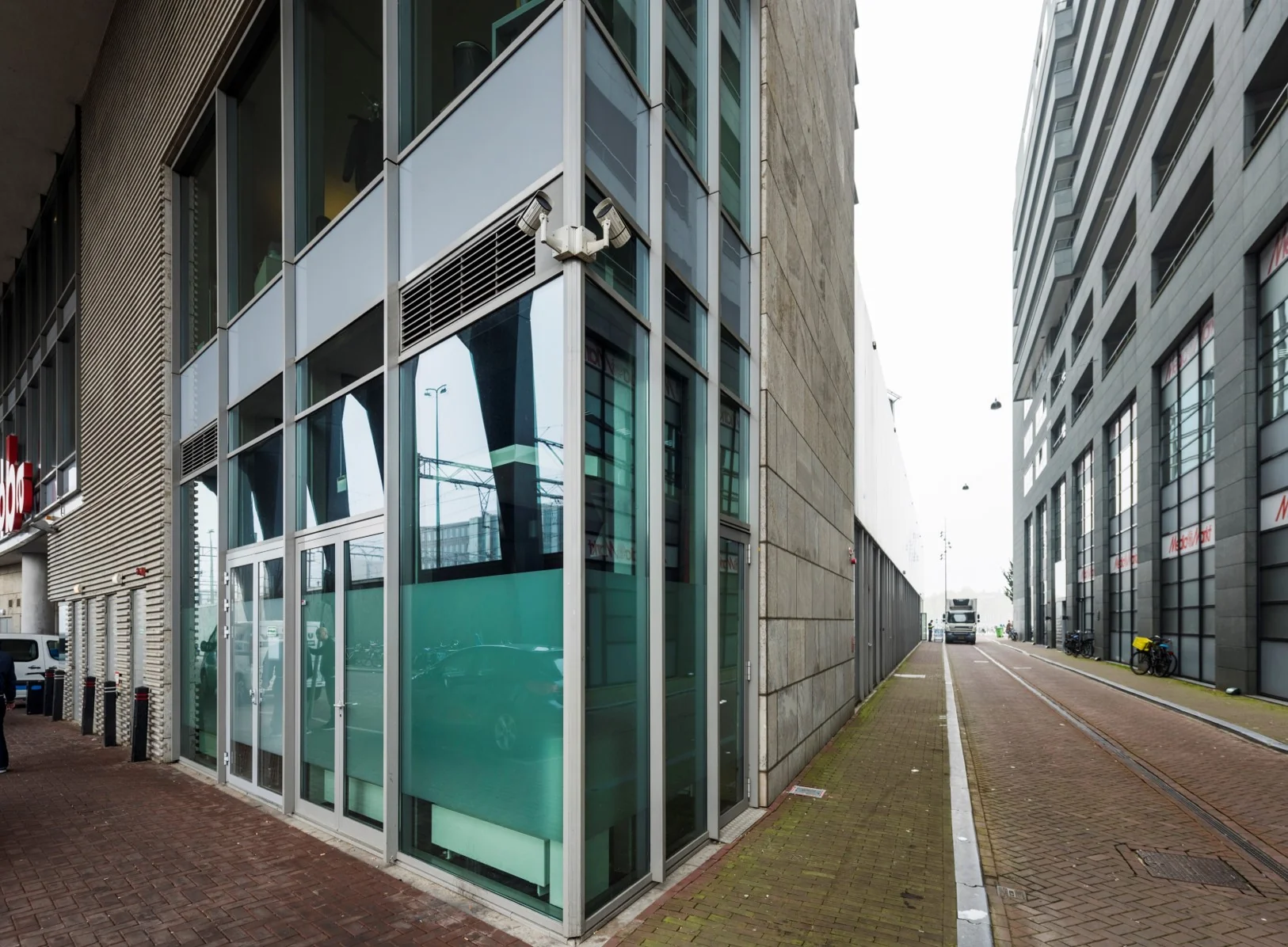 Straatbeeld van de Oosterdoksstraat in Amsterdam met moderne kantoorgebouwen en een smalle doorgang tussen de panden.