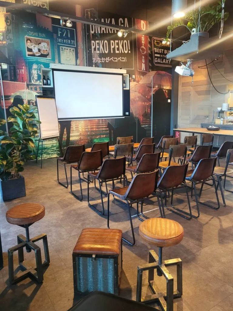Een moderne vergaderruimte aan de Oosterdoksstraat met opgestelde stoelen, een projectiescherm en decoratieve muur met Aziatische invloeden.