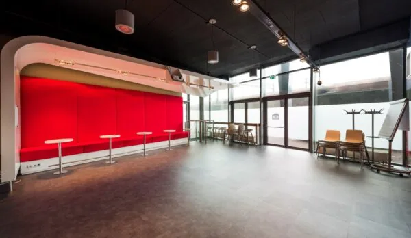 Moderne wacht- of ontmoetingsruimte aan de Oosterdoksstraat met rode wandbank, statafels, grote ramen en gestapelde stoelen.