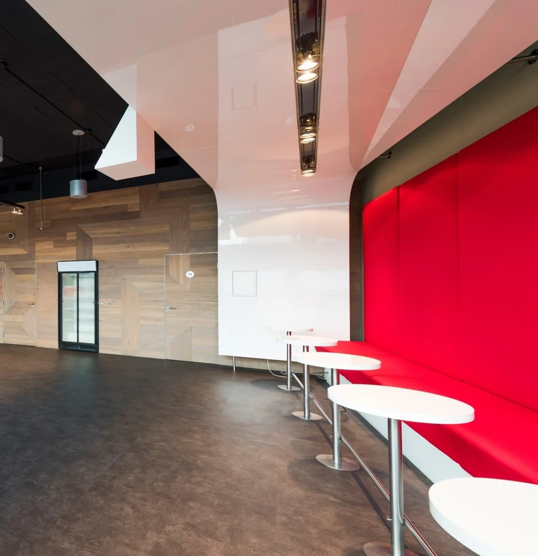 Moderne wachtruimte aan de Oosterdoksstraat met rode wandbekleding, witte zitplekken en houten muurafwerking.