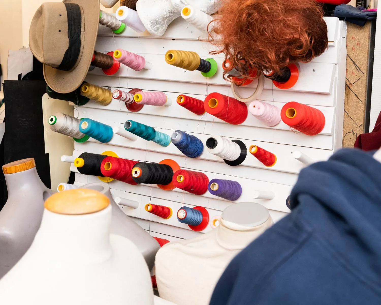 Wandrek met kleurrijke garenklossen, omringd door paspoppen en een pruik, in een creatieve werkruimte in Steiger 24, Almere.