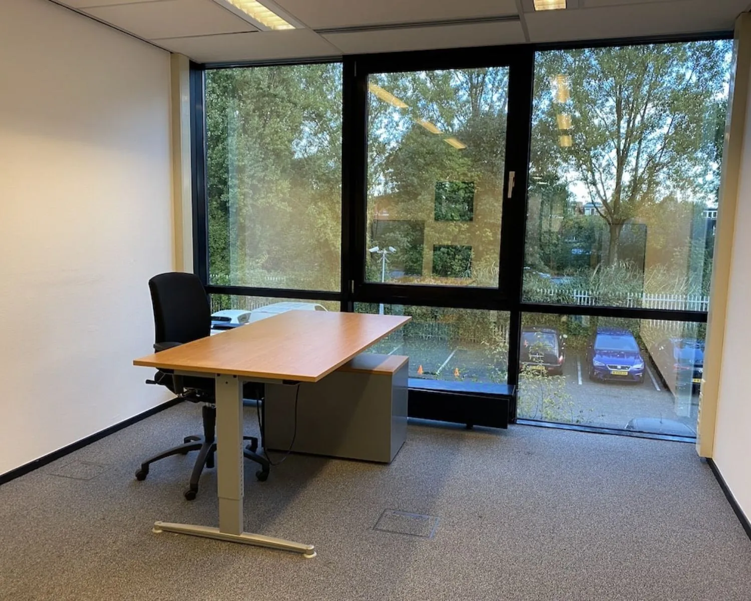 Lichte kantoorruimte met bureau en bureaustoel in het gebouw Elisabethhof in Leiderdorp, met uitzicht op parkeerplaats en bomen.