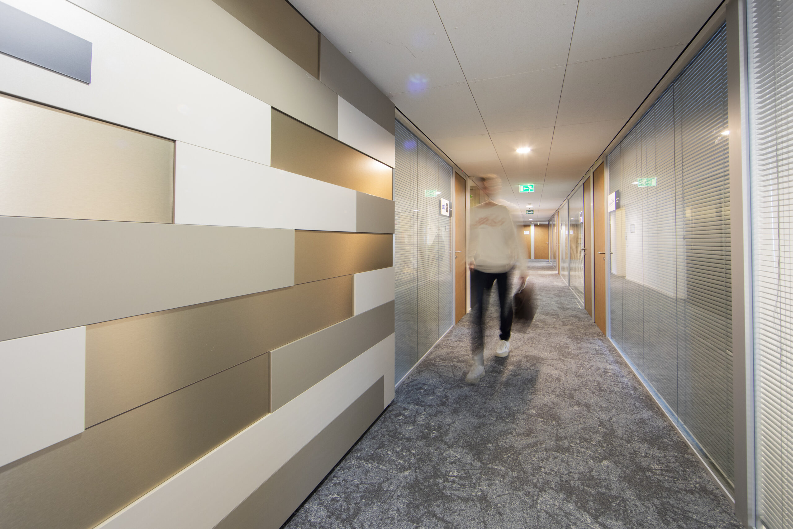 Een moderne gang op de 15e etage met geometrische wandpanelen en een persoon die langsloopt.