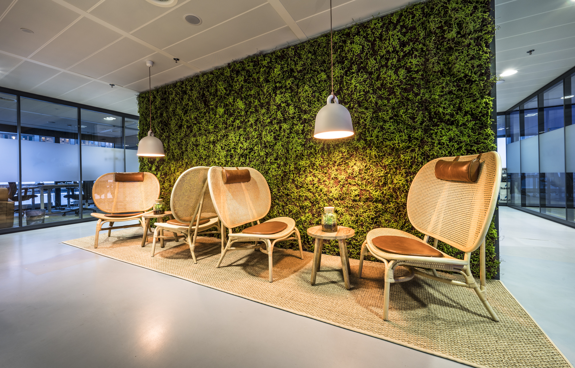 Een modern zitje met rotan stoelen en een moswand in een kantooromgeving.
