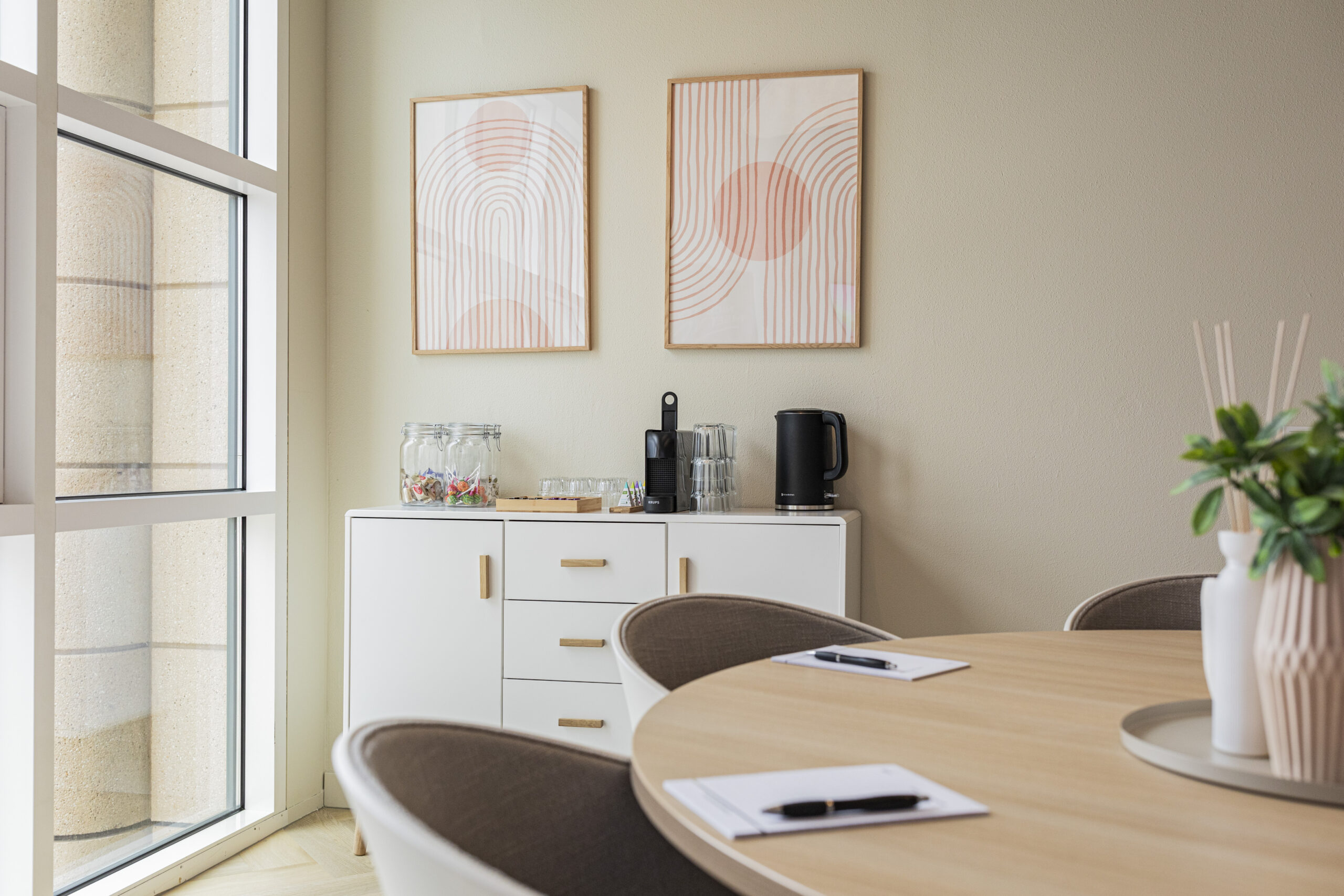 Stijlvol ingericht kantoor met een ronde tafel en een minimalistisch dressoir met kunst aan de muur.