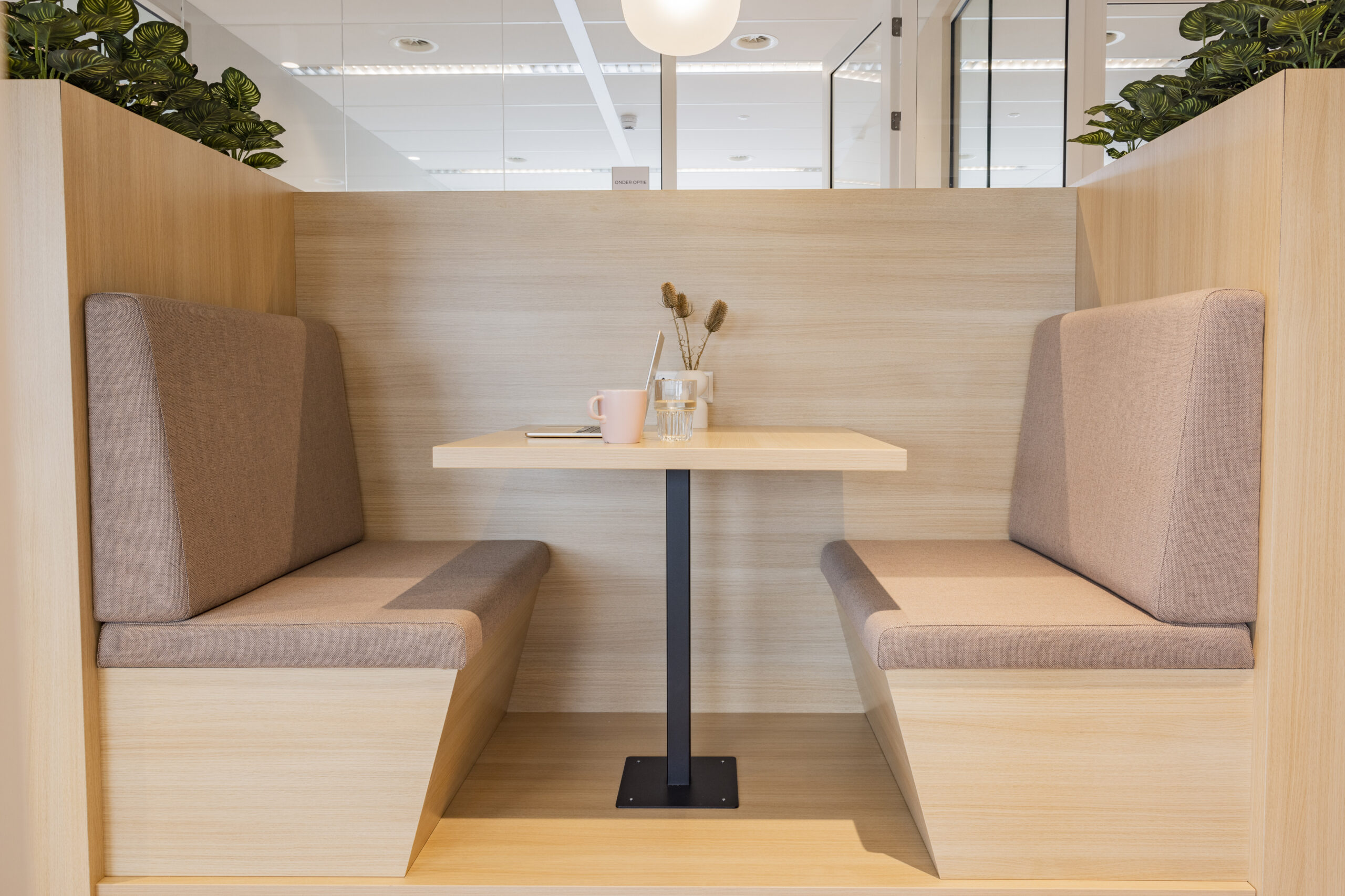 Een moderne werkplek met houten zitbanken en een tafel, versierd met planten en bureaubenodigdheden.
