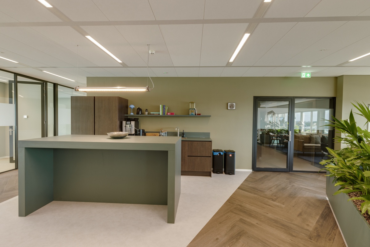 Moderne kantoorruimte met een keukenblok, groene muur, en planten.
