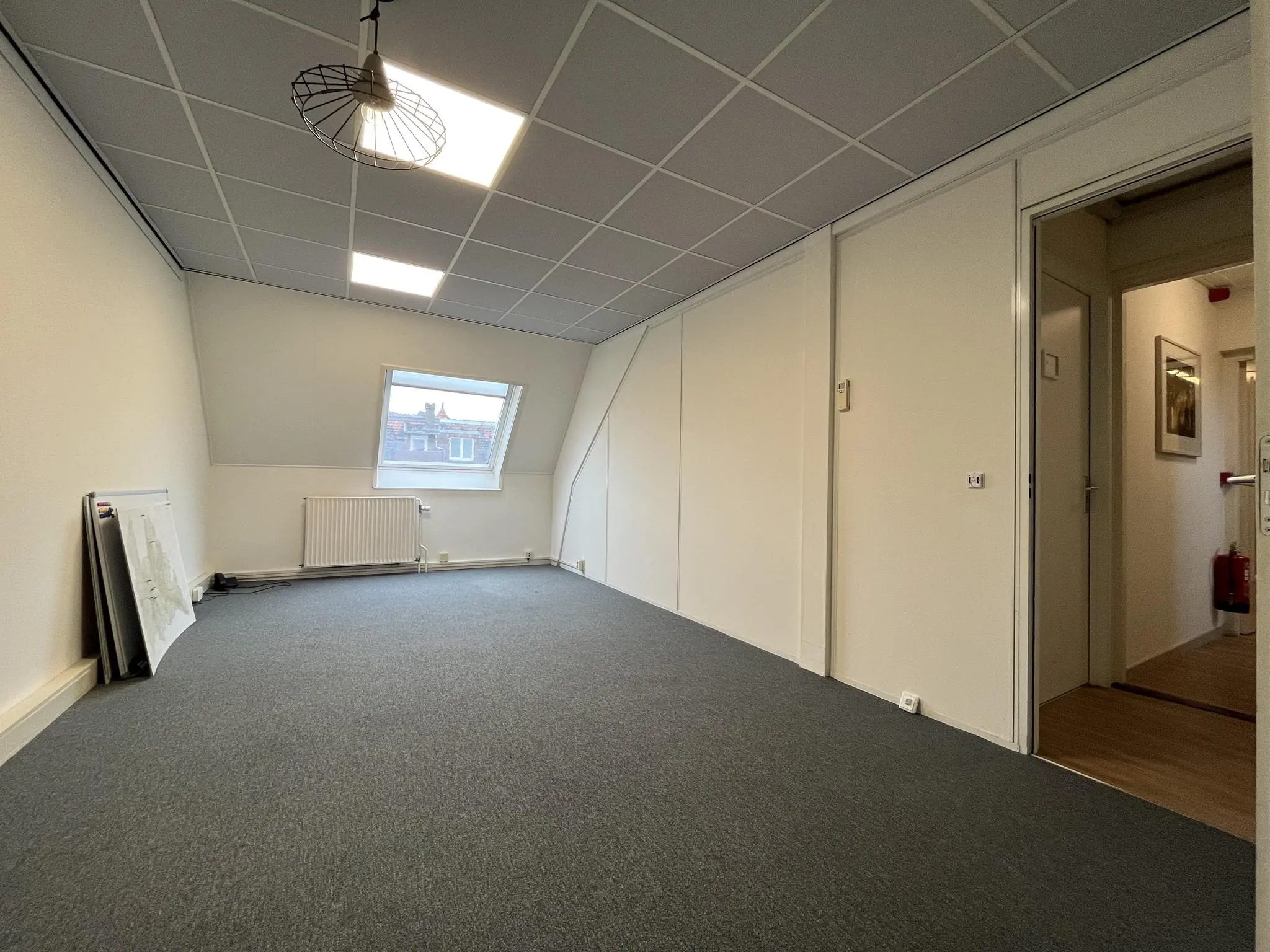 Leeg kantoorruimte op de Ramstraat met schuin dak, raam en systeemplafond.