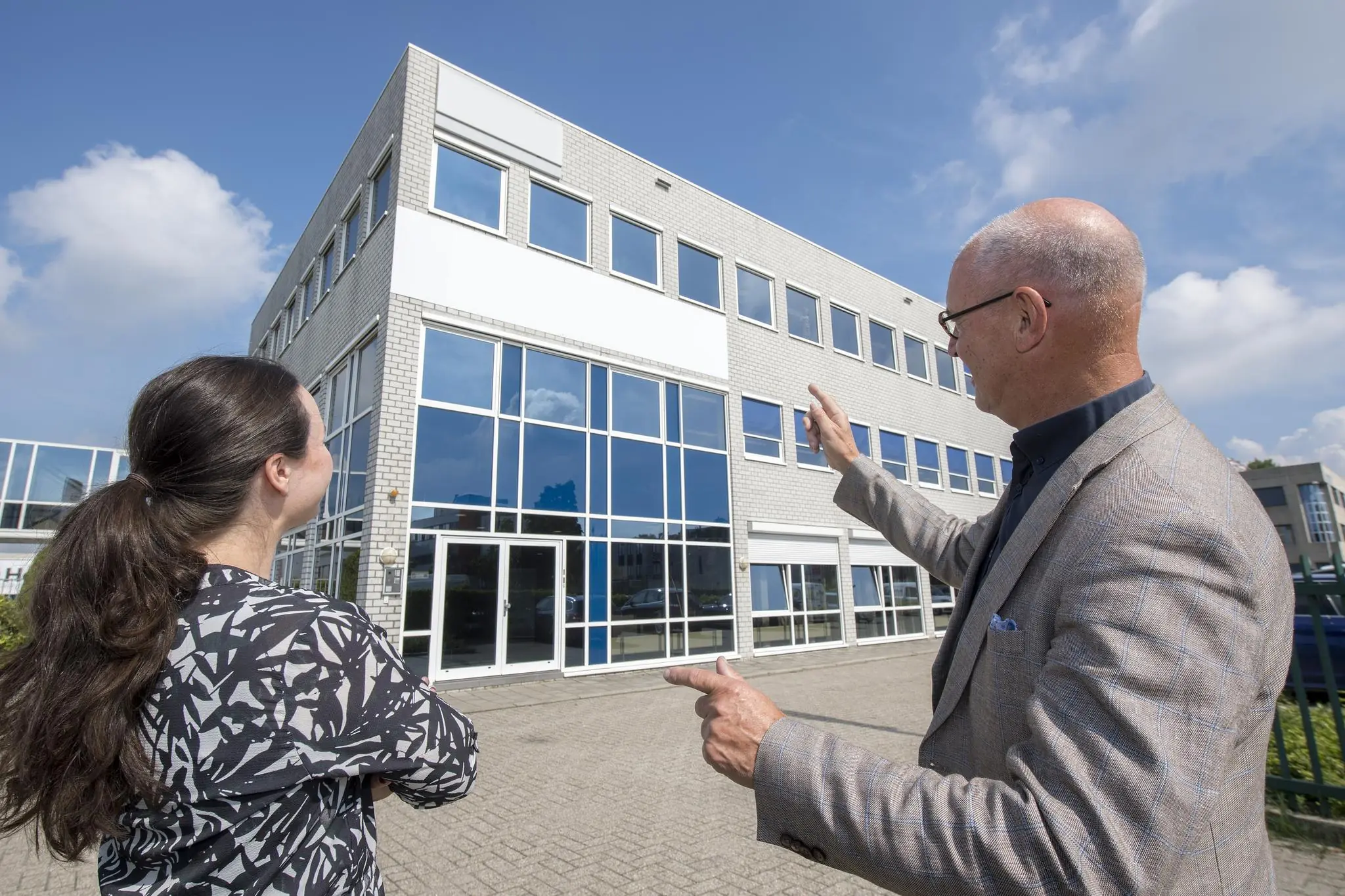 Twee mensen staan buiten en kijken naar een modern kantoorgebouw van Witboom op een zonnige dag.