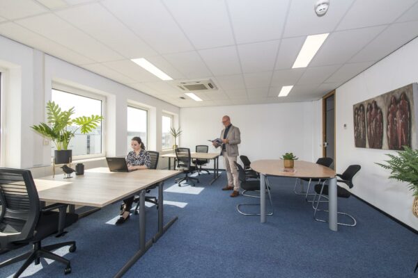 Licht en modern kantoor met een vrouw werkend aan een laptop en een man die een tijdschrift leest.