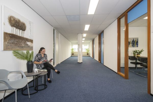 Vrouw leest een tijdschrift in een wachtruimte van een kantoor, met het schilderij 'Witboom' aan de muur.