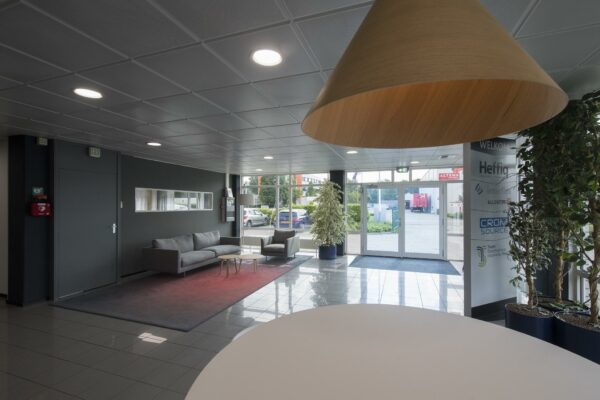 Moderne bedrijfsentree met zithoek, grote hanglamp, planten en glazen deuren naar buiten bij Witboom.
