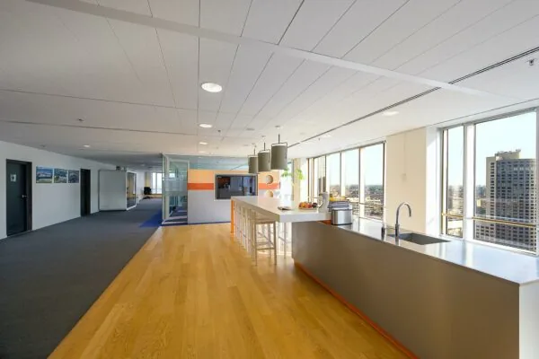 Moderne kantoorkeuken met een lang aanrecht, hoge stoelen en uitzicht op de Rotterdamse Weena-torens.