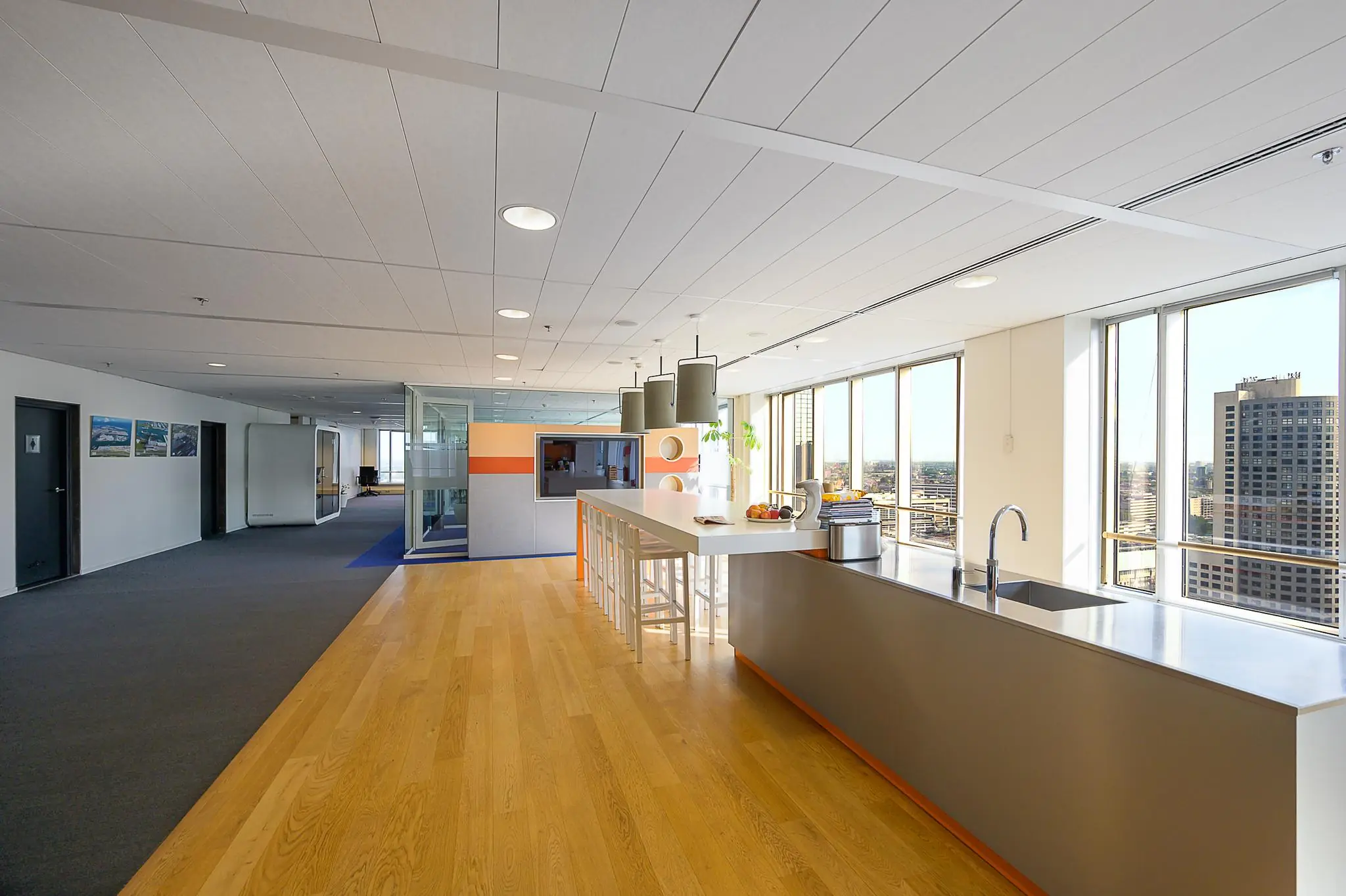 Moderne kantoorkeuken met een lang aanrecht, hoge stoelen en uitzicht op de Rotterdamse Weena-torens.