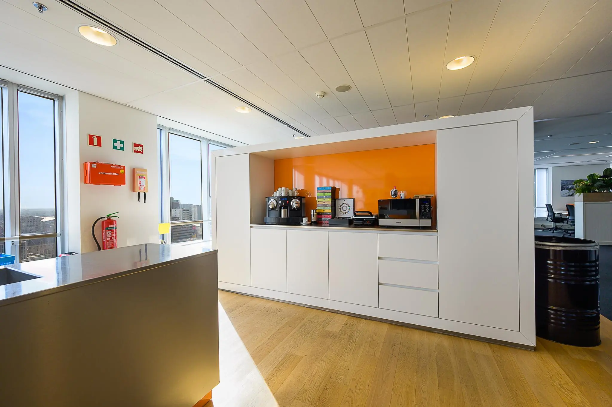 Moderne kantoorkeuken met koffiezetapparaat, magnetron en feloranje achterwand op de Weena.