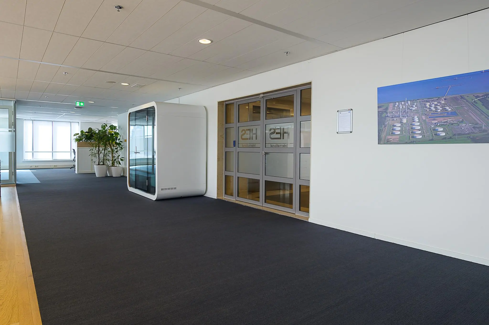 Moderne kantoorruimte aan het Weena met een akoestische belcel, glazen vergaderruimte en een groot luchtfoto-schilderij aan de muur.