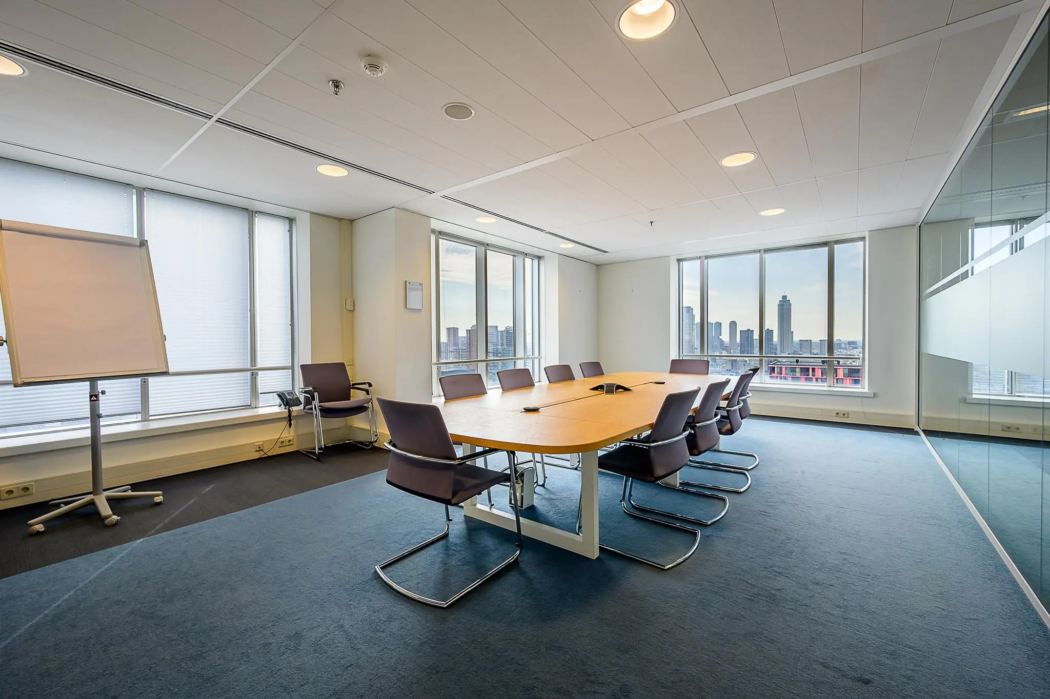 Moderne vergaderruimte met groot houten tafel, tien stoelen, flip-over en uitzicht op de Rotterdamse skyline vanaf het Weena.