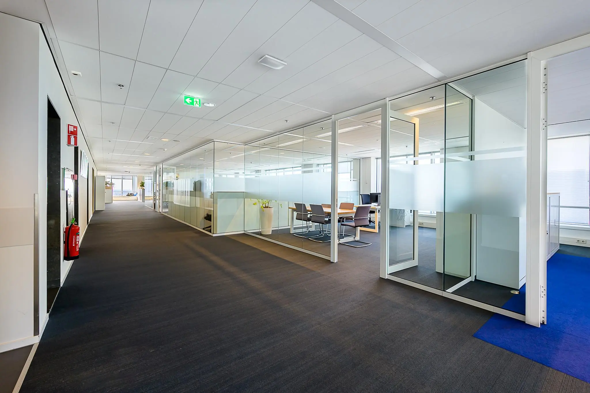 Moderne kantoorgang in gebouw Weena met glazen vergaderruimtes en strakke inrichting.