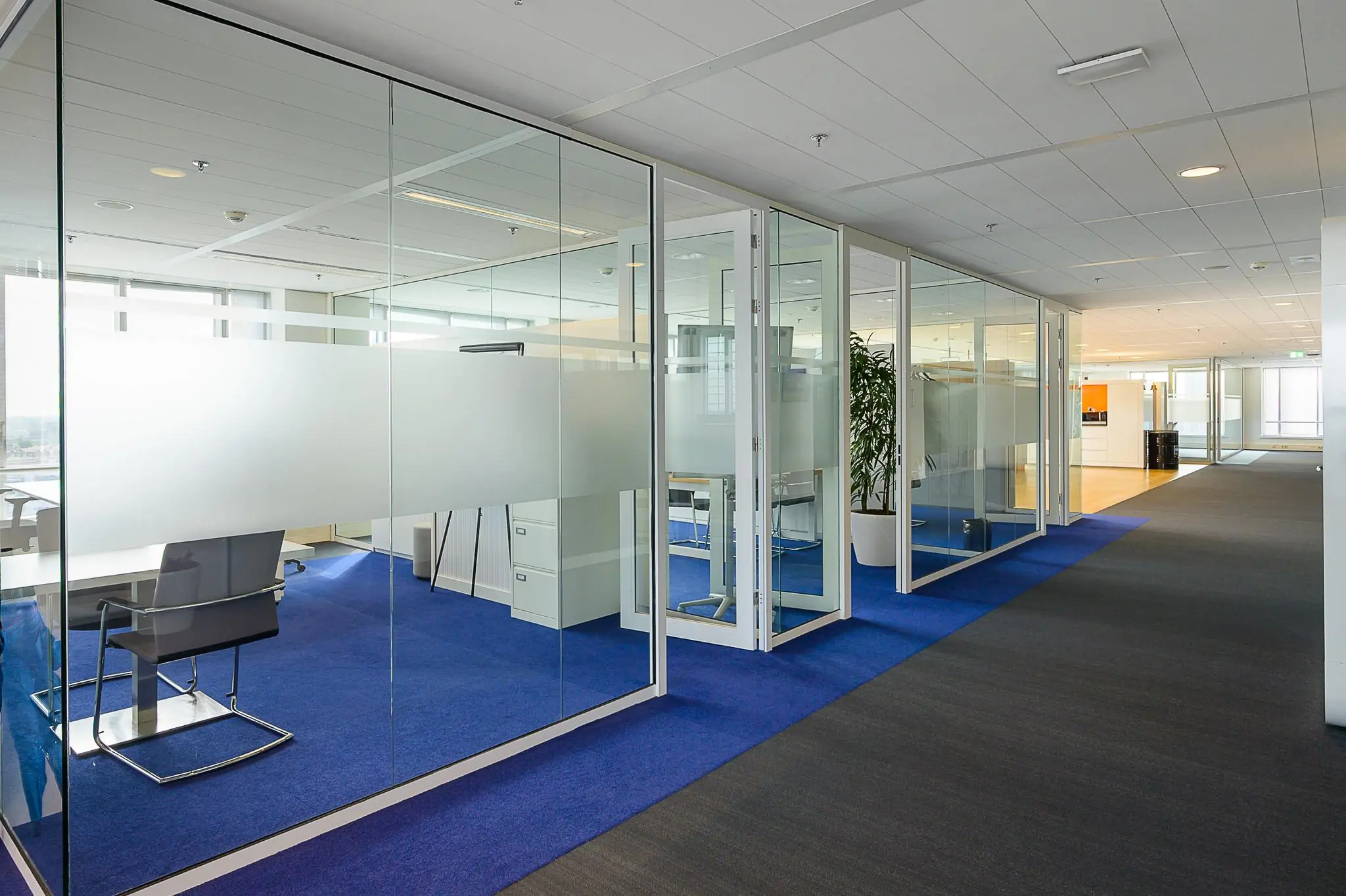 Moderne kantoorruimte aan het Weena met glazen vergaderruimtes en blauwe vloerbedekking.