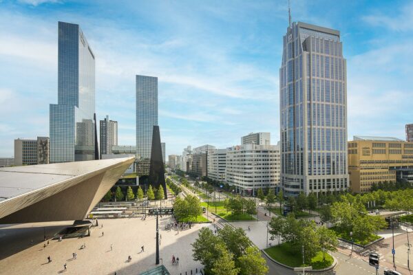 Straatbeeld van de Weena in Rotterdam met het Centraal Station en moderne hoogbouw op een zonnige dag.