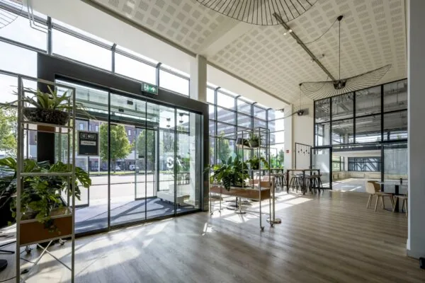 Moderne en lichte entreehal van een kantoorpand aan de Kabelweg, met veel glas, planten en zitgelegenheid.