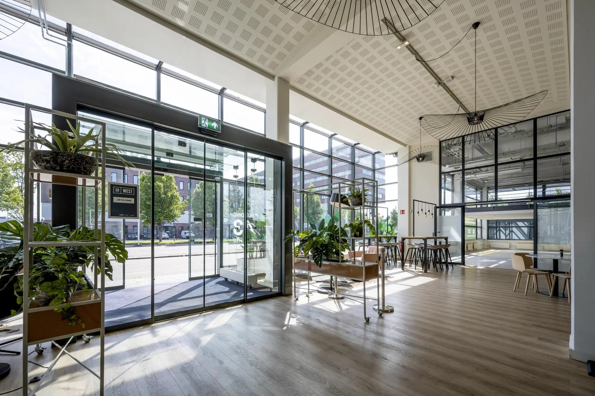 Moderne en lichte entreehal van een kantoorpand aan de Kabelweg, met veel glas, planten en zitgelegenheid.