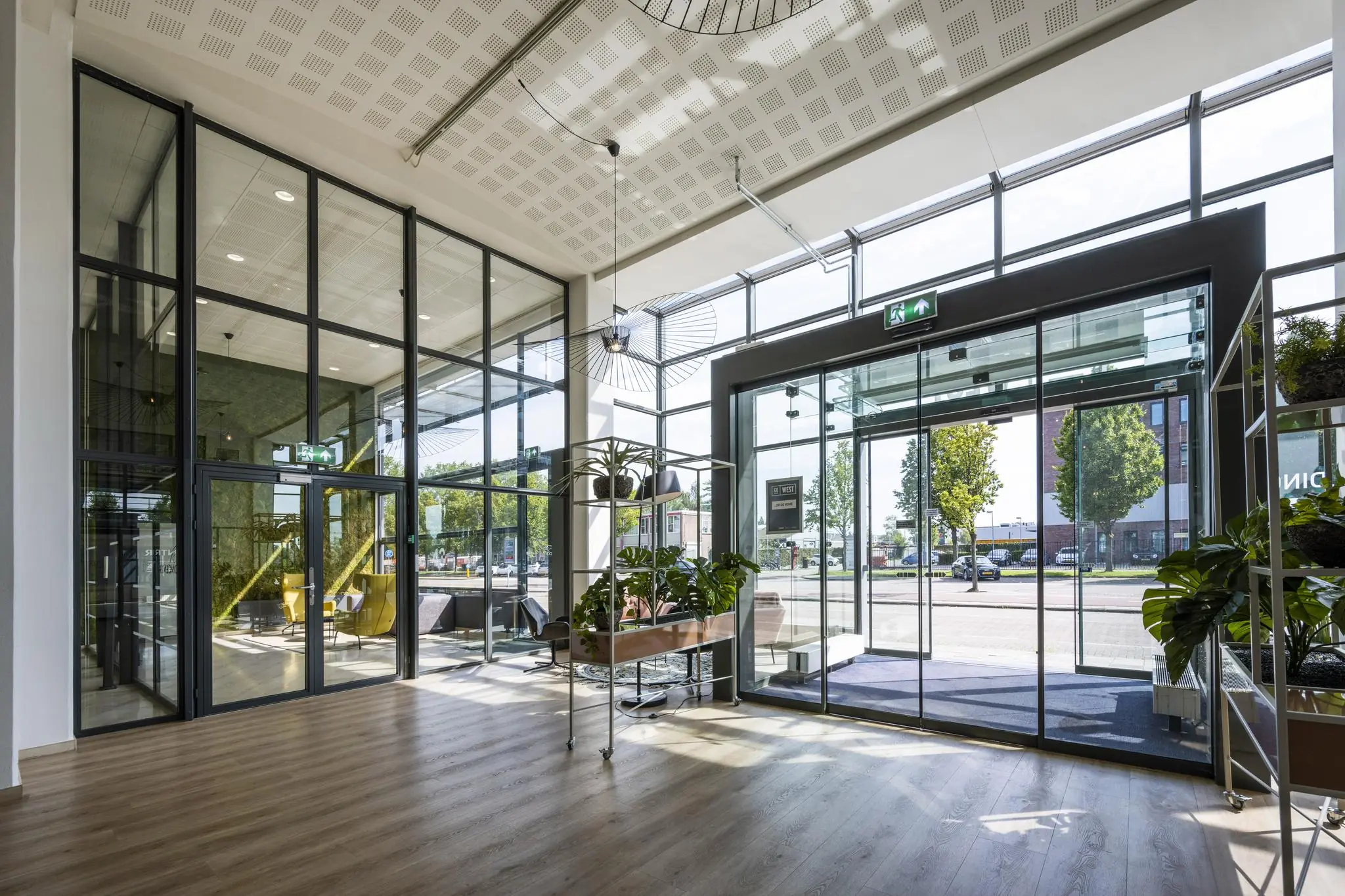 Moderne, lichte entree van een kantoorgebouw aan de Kabelweg met glazen deuren, grote ramen en veel groen.